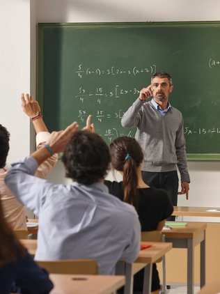 Mathematiklehrer in einem Klassenraum voller Schüler.